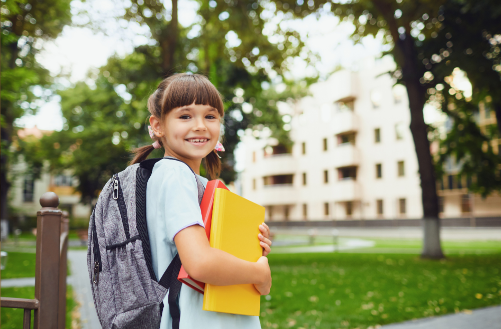 A young girl going to school wearing a backpack and carrying books