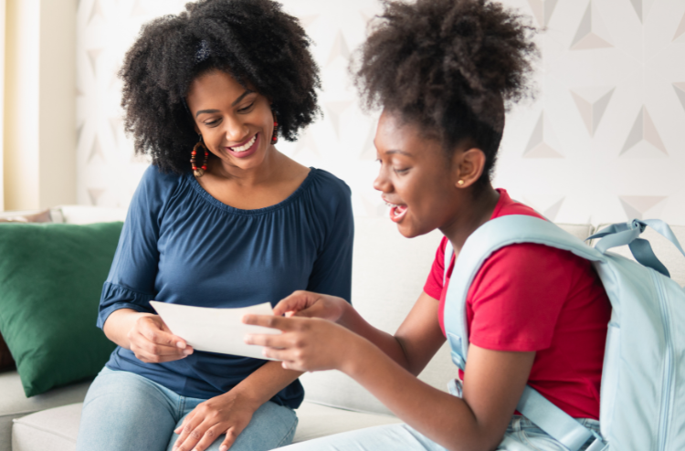A mother and her daughter looking at a school report card. They both look happy and smiling.